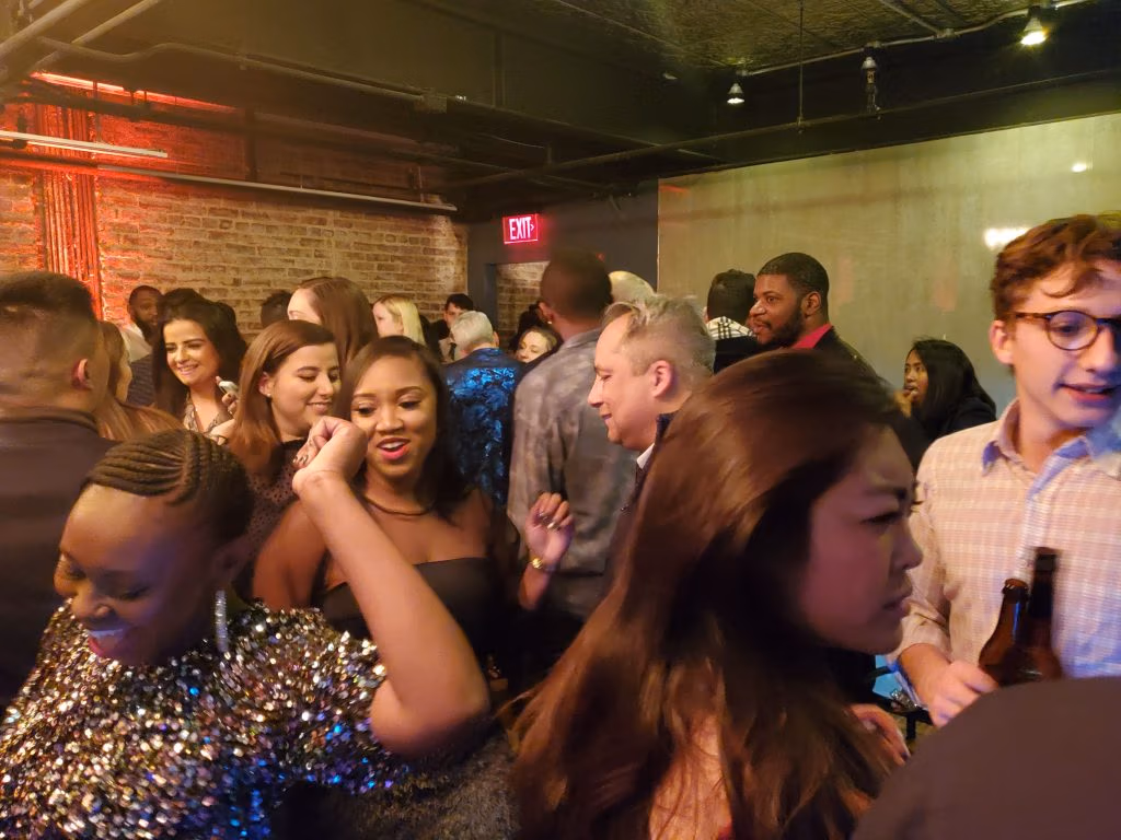 Crowded indoor party with guests dancing under red and blue lighting.