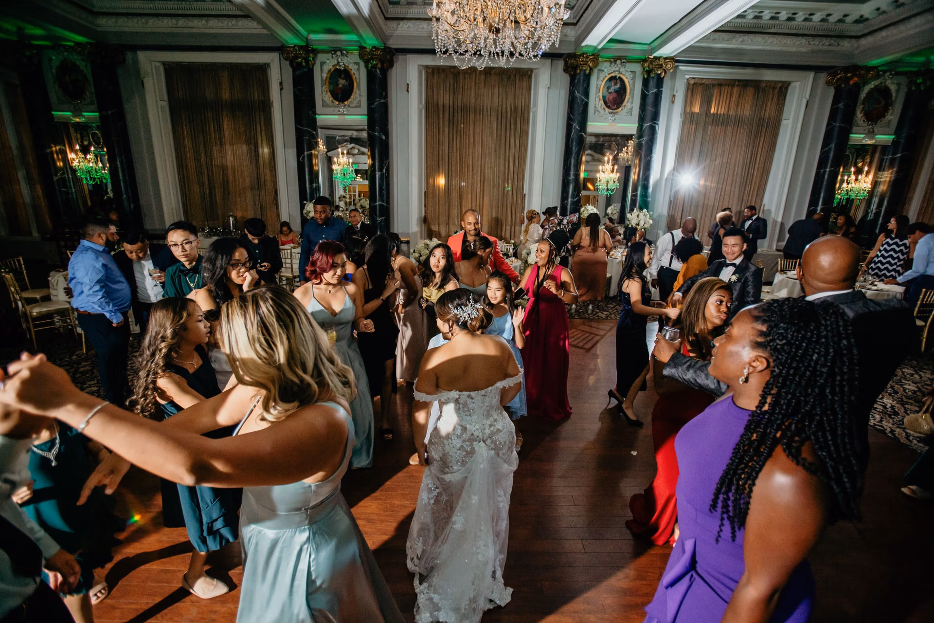 Bride and guests dancing beneath a crystal chandelier on a packed ballroom dance floor at a DC wedding reception