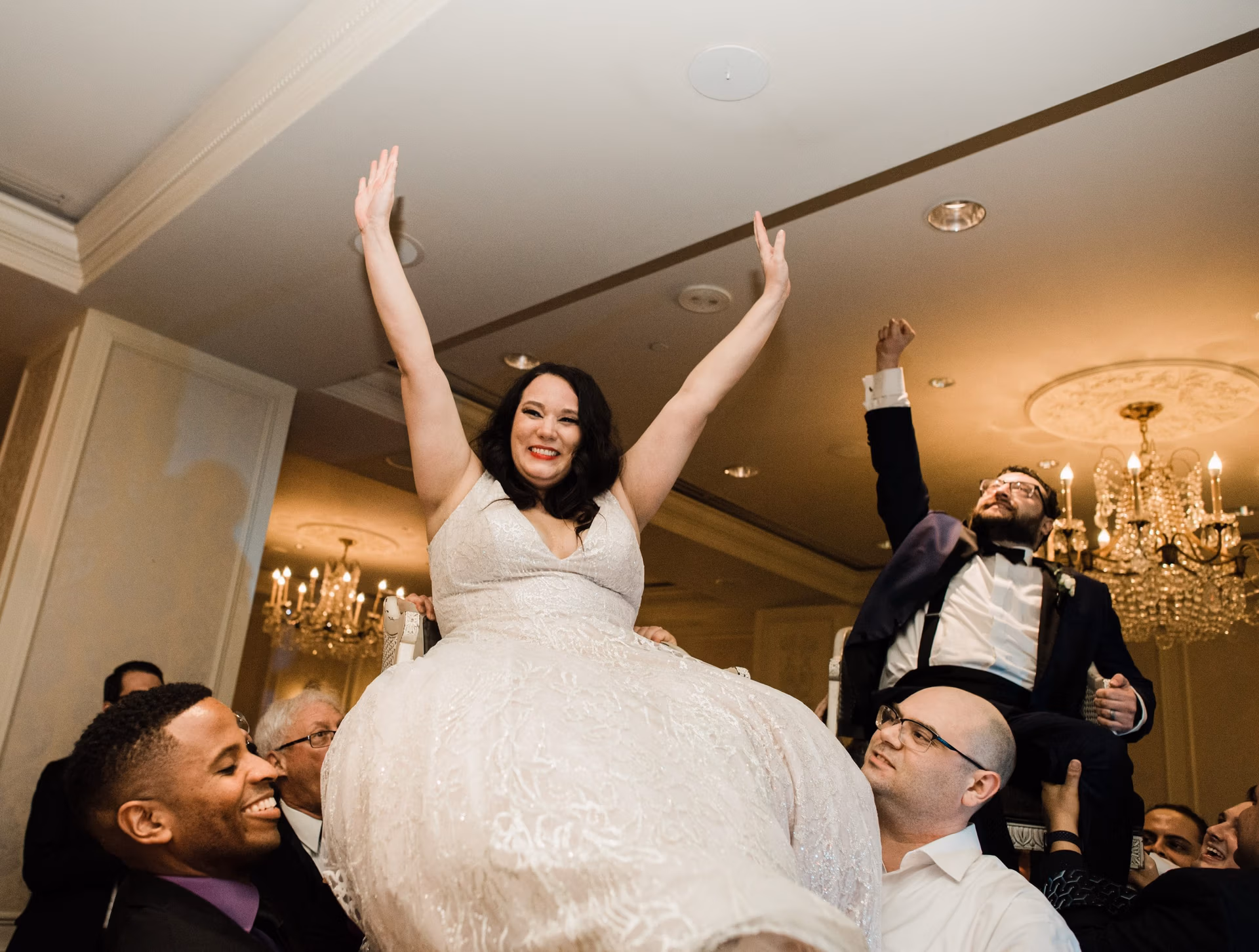 Bride raising her arms in celebration as guests dance around her at the wedding reception Bride raising her arms in celebration as guests dance around her at the wedding reception