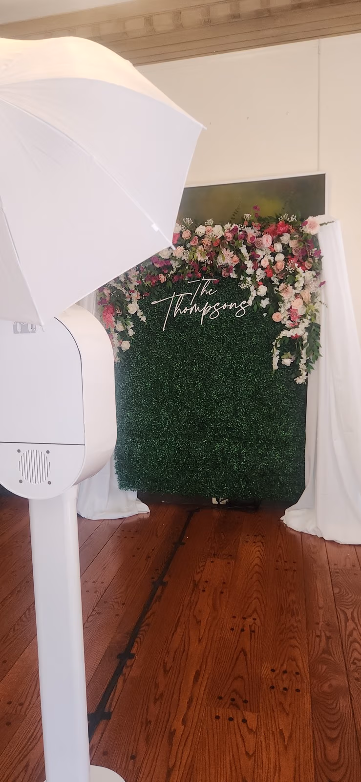 Open-air digital photo booth beside a boxwood hedge and floral backdrop at a DMV wedding